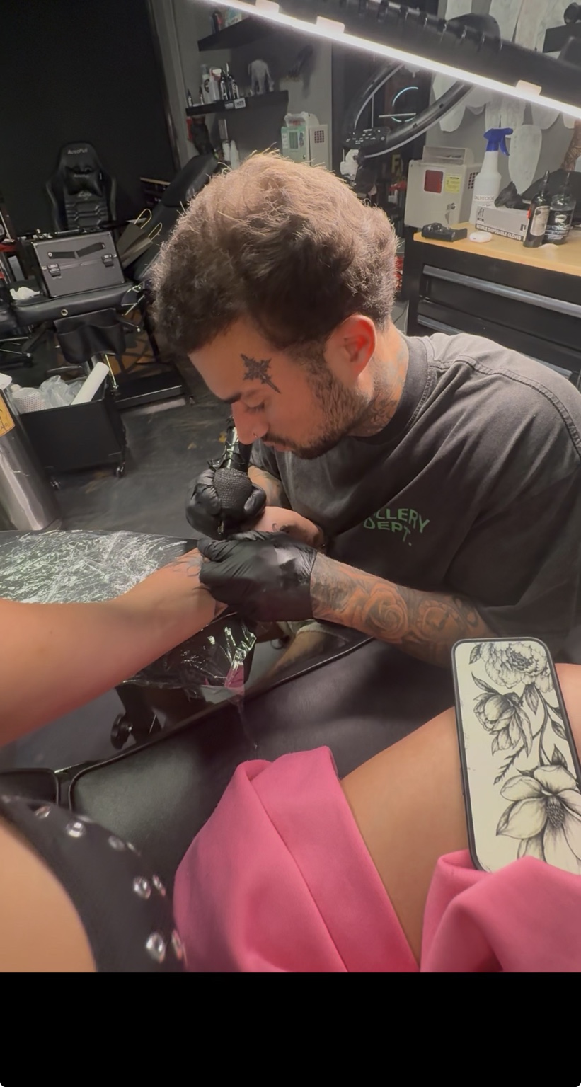 Pharaoh tattooing a client's arm in the studio