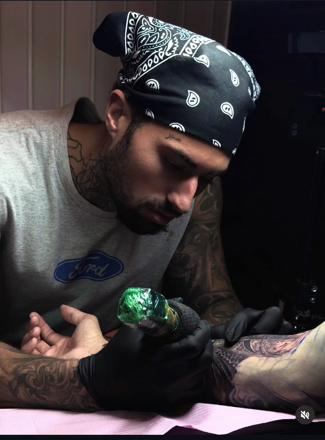 Pharaoh working on a client's forearm while wearing a paisley bandana